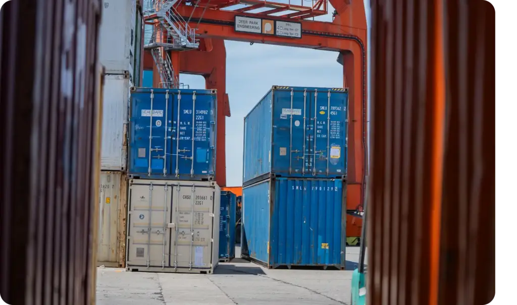 Vrachtcontainers gepositioneerd onder grote industriële cargokranen in een actieve logistieke terminal met sterke geometrische framing.