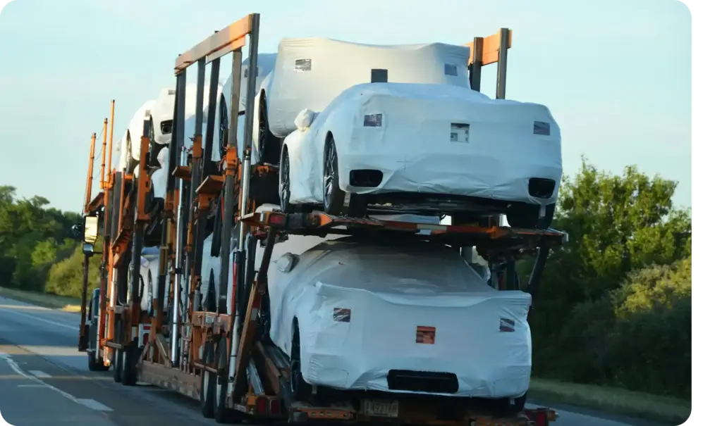 Meerdere niveaus voertuigtransport vrachtwagen die ingepakte nieuwe auto's vervoert langs een snelweg tijdens de dag.