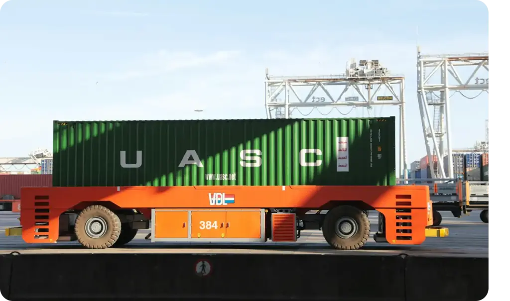 Zijaanzicht van een containertransportvoertuig dat een groene UASC-vrachtcontainer over een moderne haventerminal vervoert.